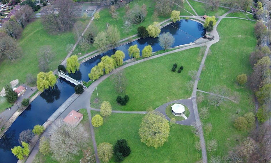 Aerial black-and-white photograph of a residential neighbourhood showing dense housing and streets. Near the center, there is a large park with two open grassy areas separated by a pathway, surrounded